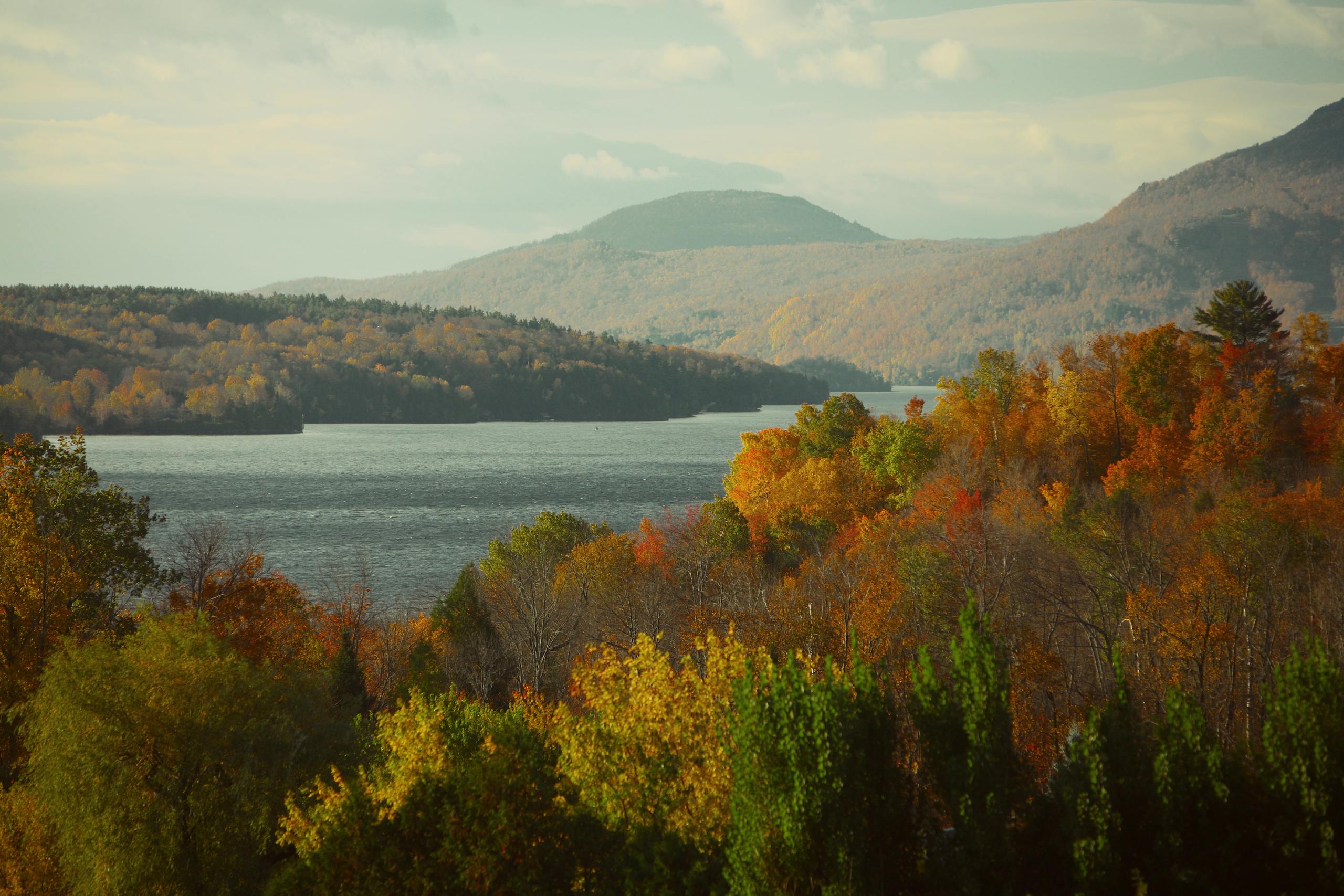 Serene lake surrounded by vibrant fall foliage and distant mountains.